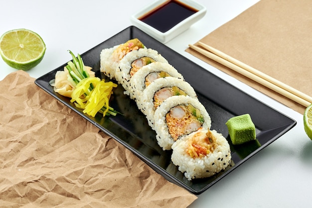Klassische japanische Sushi-Rollen mit Füllung. Uramaki mit Avocado, Rührei und Tempura-Garnelen, serviert auf einem schwarzen Teller. weiße Oberfläche