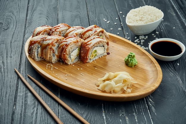 Klassische japanische Sushi-Rollen - Philadelphia-Rollen mit Frischkäse, Gurke, Avocado und Aal auf einem Bambusteller auf einem schwarzen hölzernen Hintergrund
