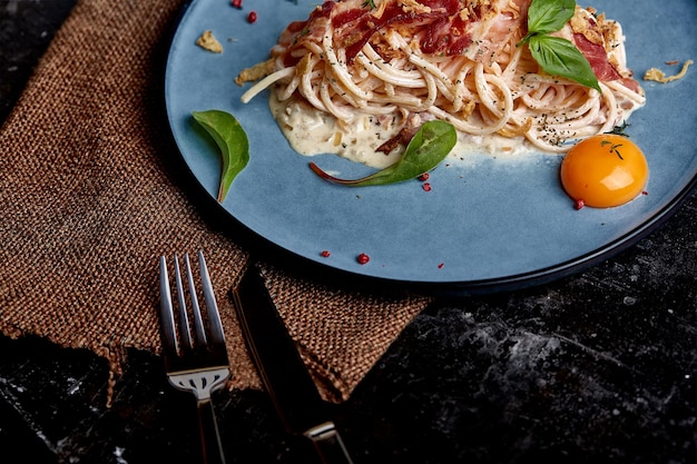 Klassische Pasta Carbonara mit Eigelb auf einem Teller Pasta auf einem blauen Teller auf dunklem Hintergrund Konzept der italienischen Küche schöne Serviergerichte in der Nähe