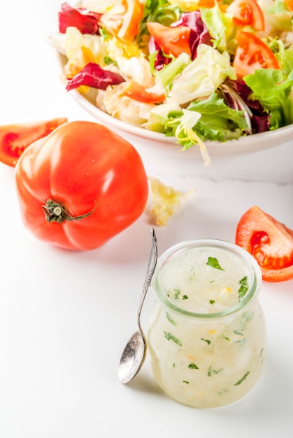 Klassische Salatsauce, hausgemachtes Ranchdressing mit Olivenölkräutern und Zitrone, mit frischem Gemüse auf weissem Marmortisch,