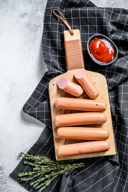 Klassische Würste aus gekochtem Schweinefleisch auf einem Schneidebrett mit Rosmarin und Gewürzen.