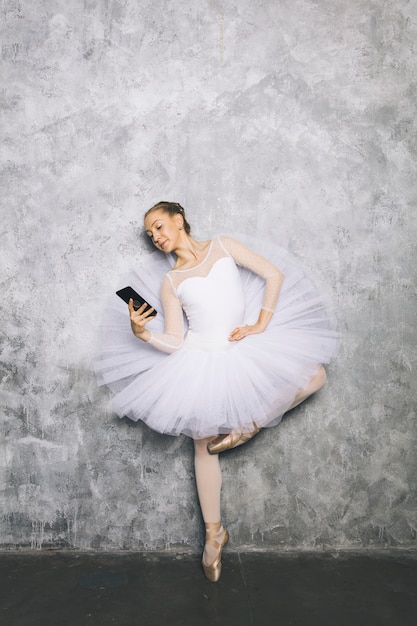 Klassischer Balletttänzer der jungen Ballerina, der Handy gegen rustikale Wand verwendet