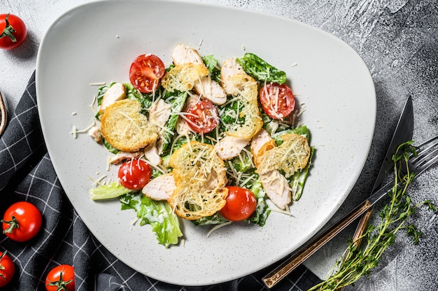 Klassischer Caesar-Salat mit gegrillter Hähnchenbrust, Parmesan, Wachteleiern, Tomaten und Römersalat. Weißer Hintergrund. Draufsicht