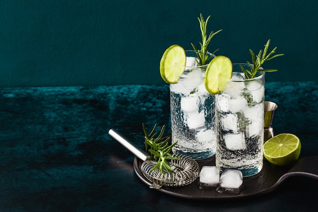 Klassischer Gin Tonic Cocktail mit Rosmarinzweigen in hohen Gläsern auf einem Tisch mit Barzubehör