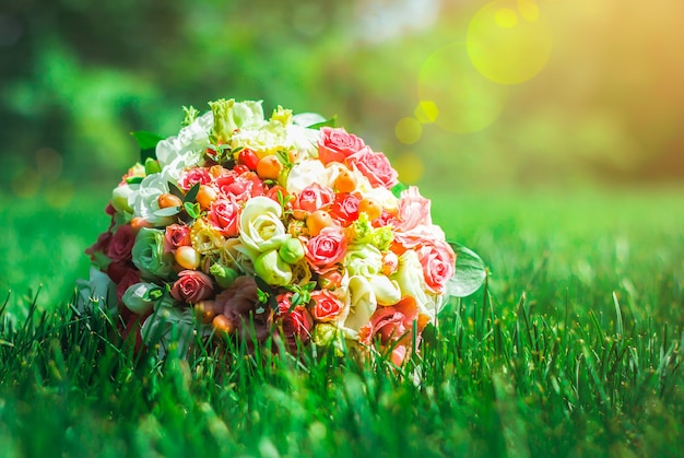 Klassischer Hochzeitsstrauß aus Rosen, Eustoma und Freesie liegt im dichten Gras. Hellgrünes und smaragdgrünes Sommerfoto. Hochzeitsdetails.