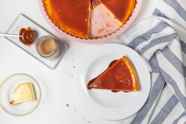 Klassischer Käsekuchen mit Karamellsauce auf weißem Teller auf grauem Hintergrund.