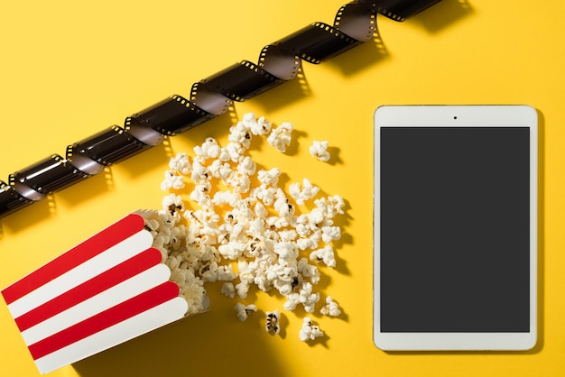 Klassischer Popcorn-Eimer und Tablet-Computer mit leerem Bildschirm auf gelbem Hintergrund