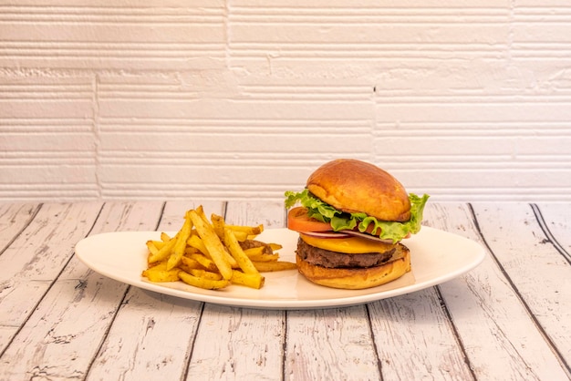 Klassischer Rindfleischburger mit roten Zwiebeln, Tomatenscheiben, Cheddar-Käse und Eisbergsalat auf einem weißen Tablett und dazu Pommes Frites