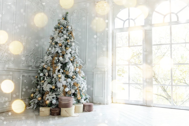 Klassischer Weihnachtsneujahrs verzierter Innenraum Baum des neuen Jahres. Weihnachtsbaum mit Goldschmuck. Moderne weiße Innenarchitekturwohnung im klassischen Stil, großes Fenster. Heiligabend zu Hause.