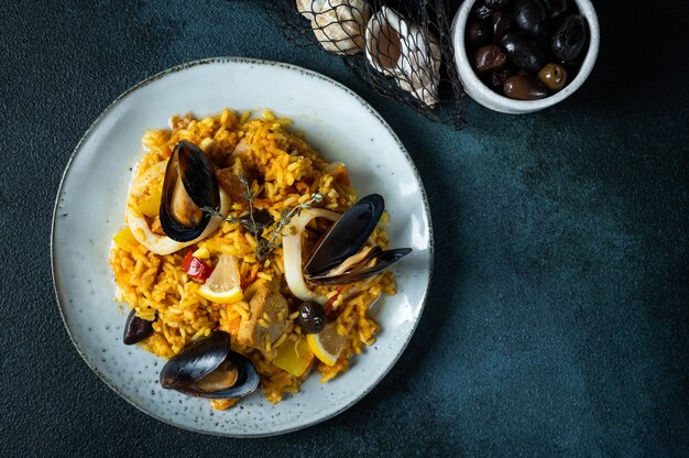 Klassisches Gericht aus Spanien, Paella mit Meeresfrüchten in der Platte auf Draufsicht des blauen Hintergrundes. Spanische Paella mit Garnelen, Klammern, Muscheln und frischer Zitrone. Spanisches Essen. Komfort Essen. Reis mit Meeresfrüchten.