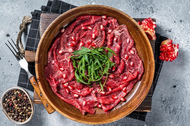 Klassisches Rinderfleisch-Carpaccio mit Rucola und Granatapfelkernen Grauer Hintergrund Ansicht von oben