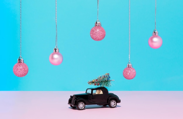 Klassisches schwarzes Auto mit Weihnachtsbaum und rosa Weihnachtskugeln auf blauem Hintergrund