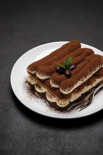 Klassisches Tiramisu-Dessert auf Keramikplatte auf dunkler Betonoberfläche