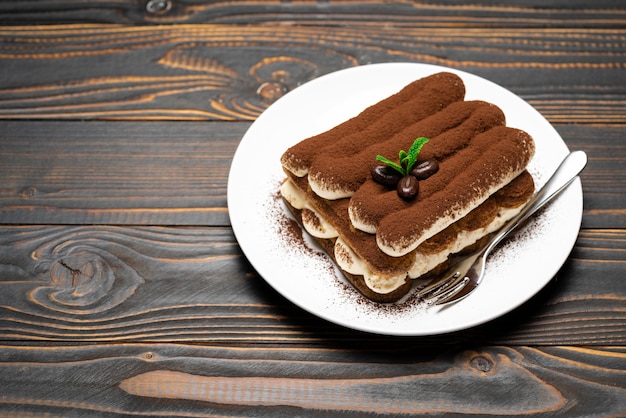 Klassisches Tiramisu-Dessert auf Keramikplatte auf hölzernem Hintergrund