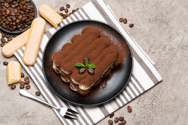 Foto klassisches tiramisu-dessert und savoiardi-kekse auf keramikplatte auf betontisch