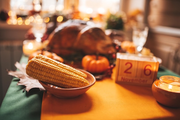 Klassisches USA Thanksgiving Day Dinner mit festlichem Herbstdekor und Kerzen. Familienesszimmertisch mit köstlichem golden gebratenem Truthahn auf Platte mit Holzblockkalender, kleinen Kürbissen und Mais