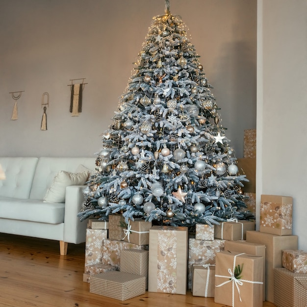 Foto klassisches weihnachtsneujahr dekorierter innenraum. weihnachtsbaum mit gold- und silberverzierungen. ein großer schön geschmückter weihnachtsbaum mit geschenkboxen steht im zimmer. heiligabend zu hause.