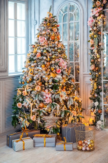 Klassisches weißes Weihnachtsinterieur. schneebedeckter Baum mit Geschenken und blinkender Girlande geschmückt