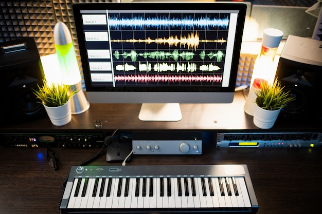 Klaviertastatur und Computerbildschirm mit Wellenform-Klangvisualisierung am Arbeitsplatz eines modernen Musikers oder DJs im Studio