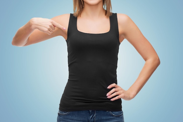 Foto kleidungsdesign, mode, werbung und people-konzept - nahaufnahme einer frau in einem leeren schwarzen tanktop, die mit dem finger auf sich selbst über blauem hintergrund zeigt