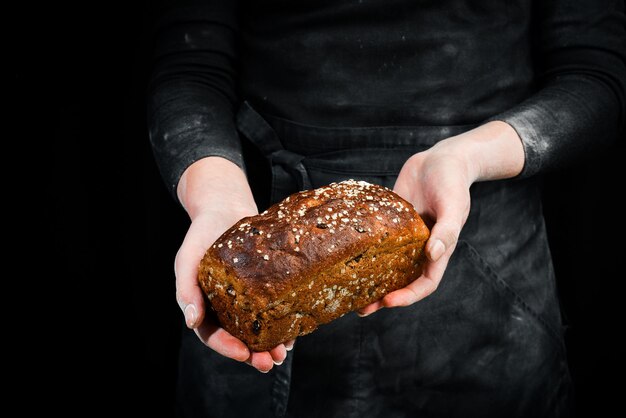 Kleiebrot mit getrockneten Früchten in Frauenhänden. Schwarzer backender Hintergrund.