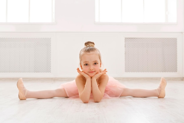 Kleine Ballerina im Split auf dem Boden, Kopienraum. Lächelndes Baby, das träumt, professionelle Balletttänzerin zu werden, klassische Tanzschule