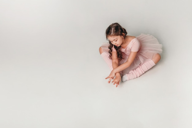 Kleine Ballerina-Tänzerin in einem rosa Ballettröckchen-Akademiestudenten, der auf weißem Hintergrund aufwirft