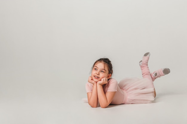 Kleine Ballerina-Tänzerin in einem rosa Ballettröckchen-Akademiestudenten, der auf weißem Hintergrund aufwirft