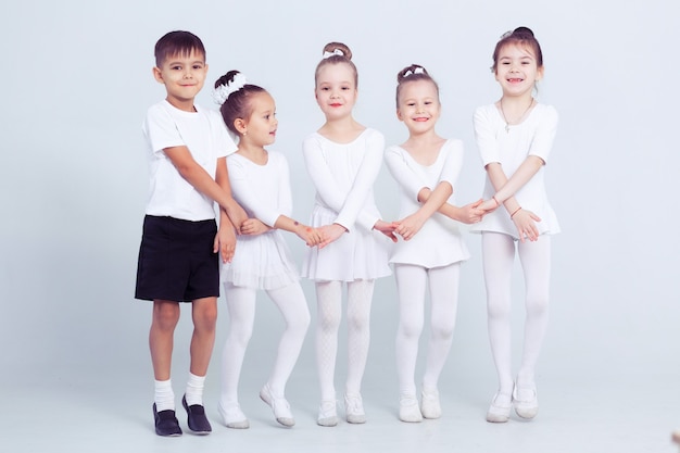 Kleine Ballerinas und Kinderballerun machen Übungen und sitzen auf dem Boden in der weißen Ballettklasse.