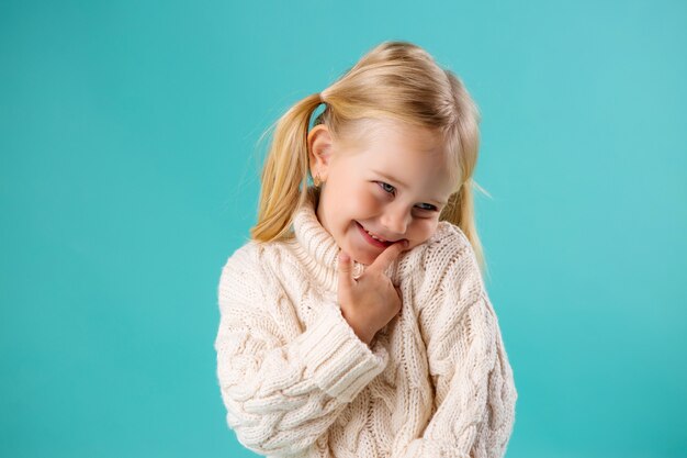 kleine Blondine in der Strickjacke lächelnd auf Blau