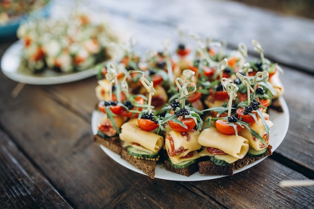 Kleine Burger mit Fleisch, Salatkäse und Tomaten auf hölzerner Platte während der Sommergrillparty draußen.