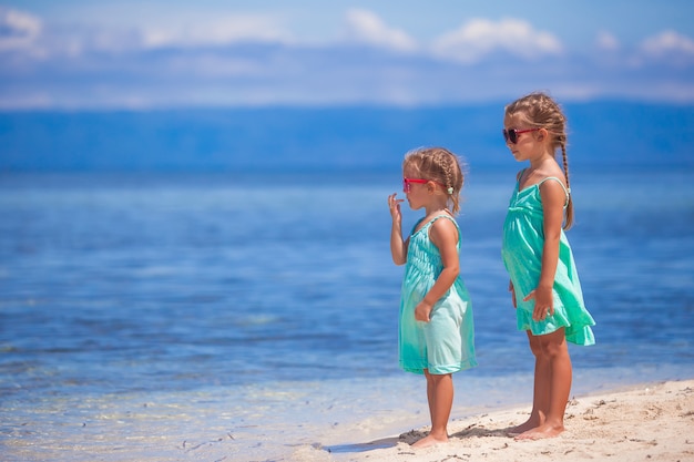 Kleine entzückende Mädchen im Türkiskleid auf weißem Strand betrachten das Meer