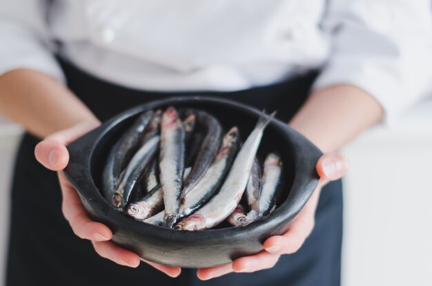 Kleine Fische in der Keramikschale über den Händen des Küchenchefs.