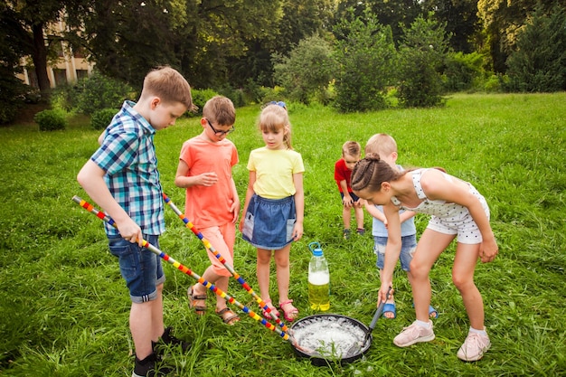 Kleine Freunde, die im Sommer auf einer Wiese trainieren, um große Seifenblasen zu machen