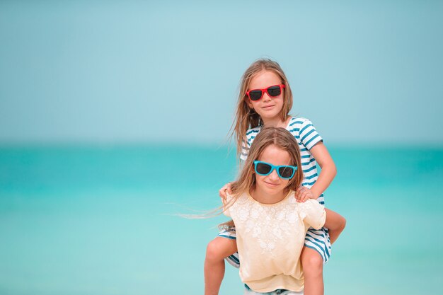 Kleine fröhliche lustige Mädchen haben viel Spaß am tropischen Strand, wenn sie zusammen spielen. Sonniger Tag mit Regen im Meer