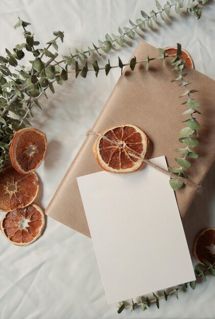 Kleine Geschäftsbox und Postkartenstillleben in weißem Hintergrund mit getrockneten Orangenscheiben und Eukalyptusblättern für umweltfreundliche Weihnachten