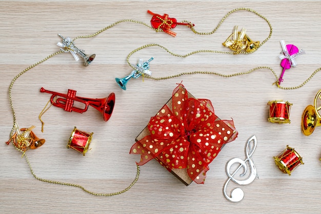 Kleine Geschenkbox mit bunter Bandfliege auf Holztisch mit kleinen dekorativen Musikinstrumenten an Heiligabend-Geburtstagsnacht oder Neujahrsfest.