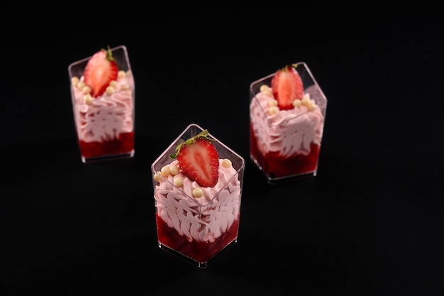 Kleine Gläser gefüllt mit geschlagener rosa Sahne und roter Marmelade, dekoriert mit Erdbeeren