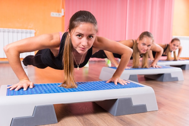 Kleine Gruppe junger Frauen, die Liegestütze oder Plank-Übungen mit Step-Plattformen in der Step-Klasse durchführen und selbstbewusst in die Kamera schauen