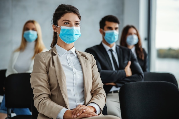 Kleine Gruppe von Geschäftsleuten mit Gesichtsmasken, die auf Seminar während des Koronavirus sitzen