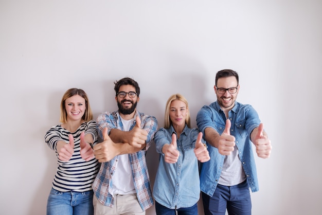 Kleine Gruppe von Menschen, die Daumen aufgeben, während sie an der weißen Wand stehen. Geschäftskonzept starten.