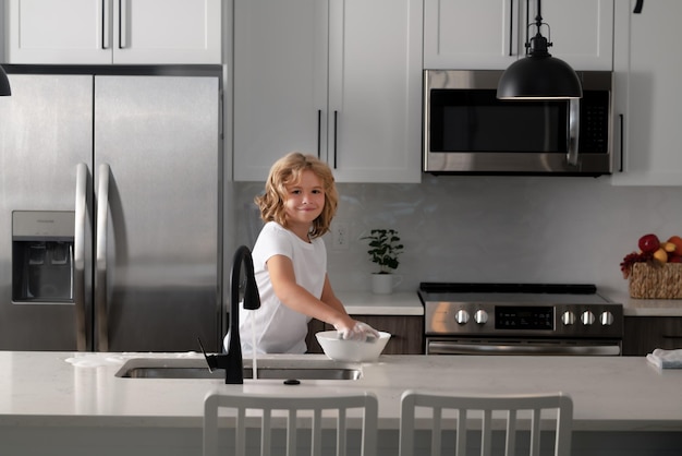 Kleine Haushälterin, Junge, wäscht Geschirr mit Wasser und Seife in der Nähe der Spüle in der Küche