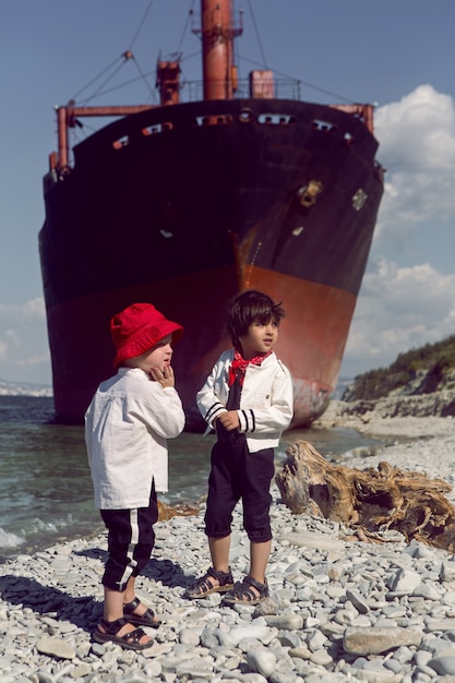 kleine Jungen stehen neben dem Schiff an der Küste