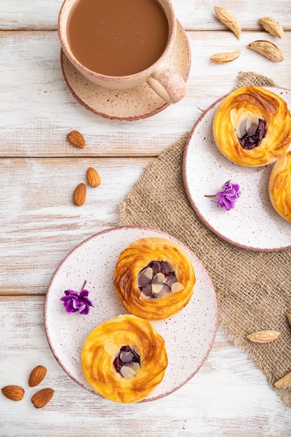 Kleine Käsekuchen mit Marmelade und Mandeln mit Tasse Kaffee auf weißem Holz