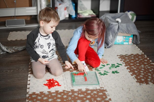 Kleine kaukasische Kinder spielen ein Brettspiel auf dem Boden in ihrem Zimmer, Lifestyle getöntes Foto zu Hause