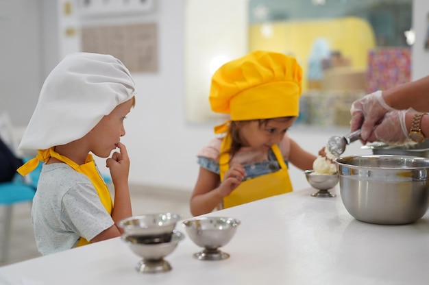 Kleine kaukasische Kinder spielen Kochkinder in einer Schürze und einer Kochmütze