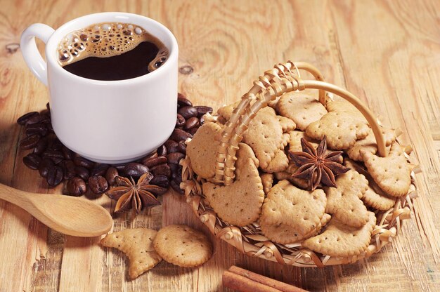 Kleine Kekse im Weidenkorb und eine Tasse heißen Kaffee auf einem alten Holztisch