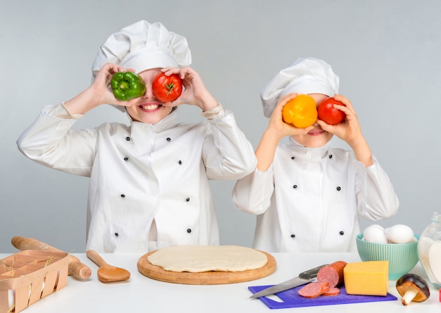 Kleine Kinder an einem Tisch, der Pizza macht