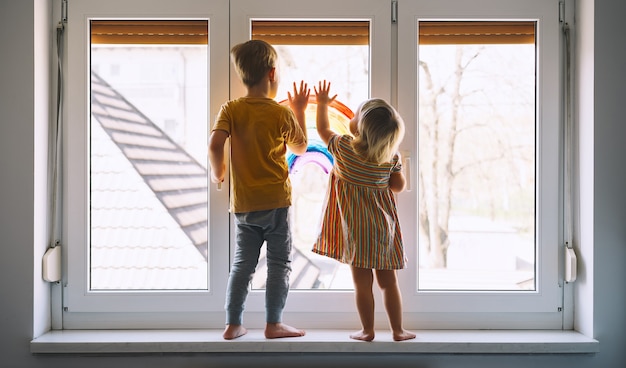 Kleine Kinder auf dem Hintergrund der Malerei Regenbogen auf dem Fenster Foto der Kinderfreizeit zu Hause