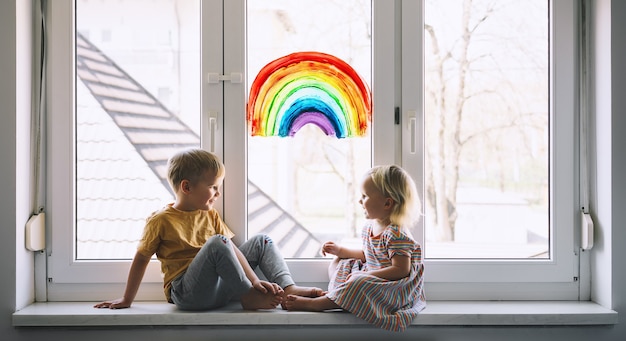 Kleine kinder auf dem hintergrund der malerei regenbogen auf dem fensterfoto der kinderfreizeit zu hause